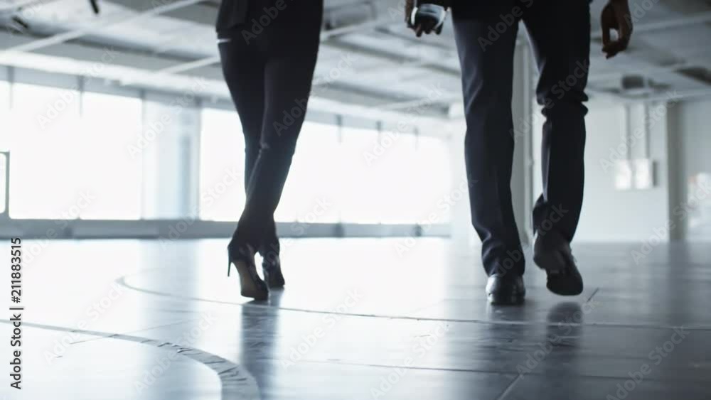 Following low-angled shot of legs of businessman and businesswoman walking together through the lobby in office center Following low-angled shot of legs of businessman and businesswoman walking together through the lobby in office center