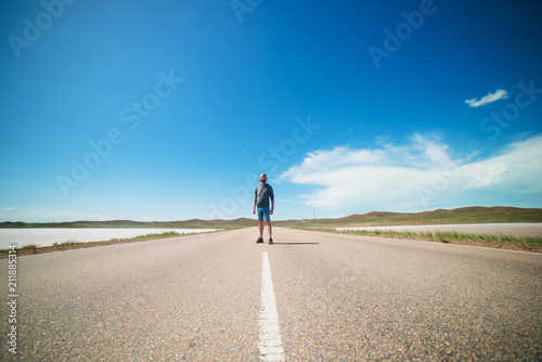 a man stands in the middle of an asphalt road in the steppe