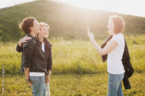 Wallpaper Mural Pretty slim mom takes pictures on smartphone her adult positive beautiful daughters walking in the park in the same clothes and white T-shirts in jeans and leather jackets Torontodigital.ca