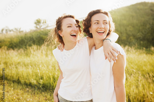 Portrait of cute young beautiful curly-haired girls sisters standing into the distance dressed in a white T-shirt posing against a green hill photo