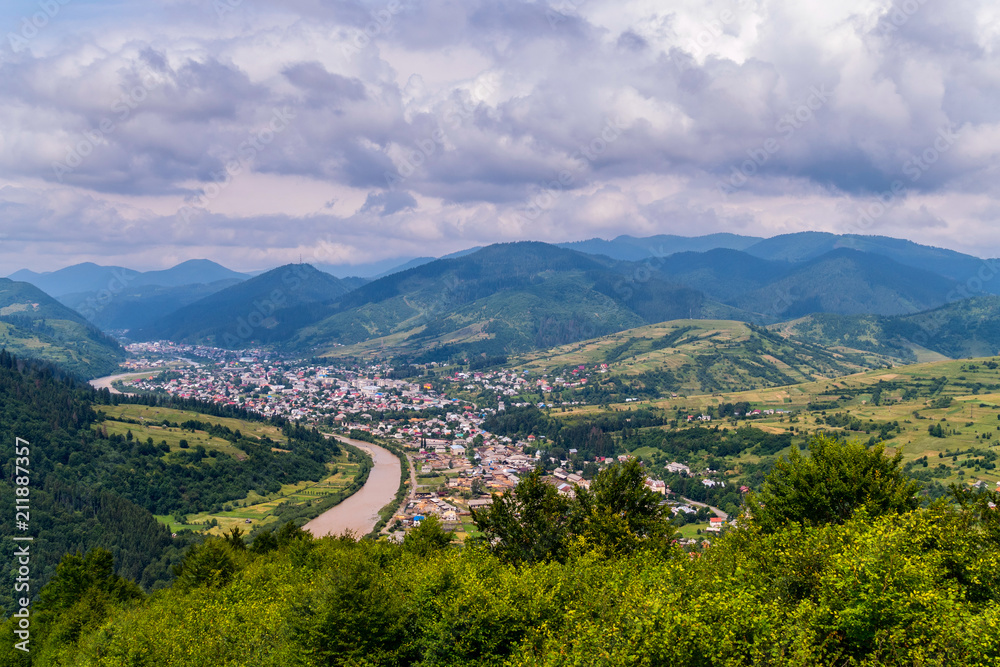 A beautiful town on the bank of a river surrounded by green forests and high mountains