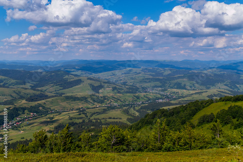 panorama with green mountain ranges and small houses in a valley under a cloudy sky © adamchuk_leo