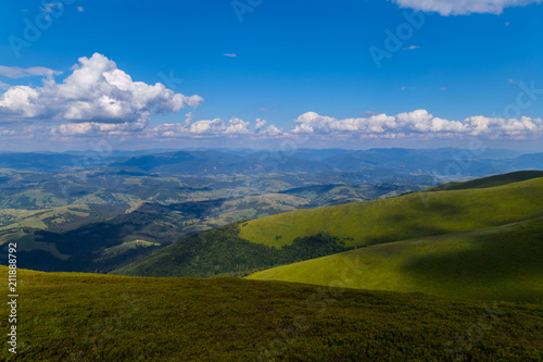 covered with low shrubs mountain slope against the background of distant peaks under clouds in the blue sky. Carpathians
