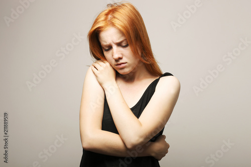 Beautiful fragile redheaded young woman in the dark. Sad frightened girl scared of abuse. Nonverbal behavior, body language. Red hair female looking stressed out & depressed. Background, close up.
