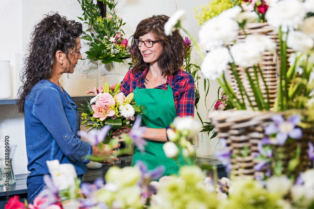 Floristin verkauft einer Kundin lächelnd einen Blumenstrauss im Laden