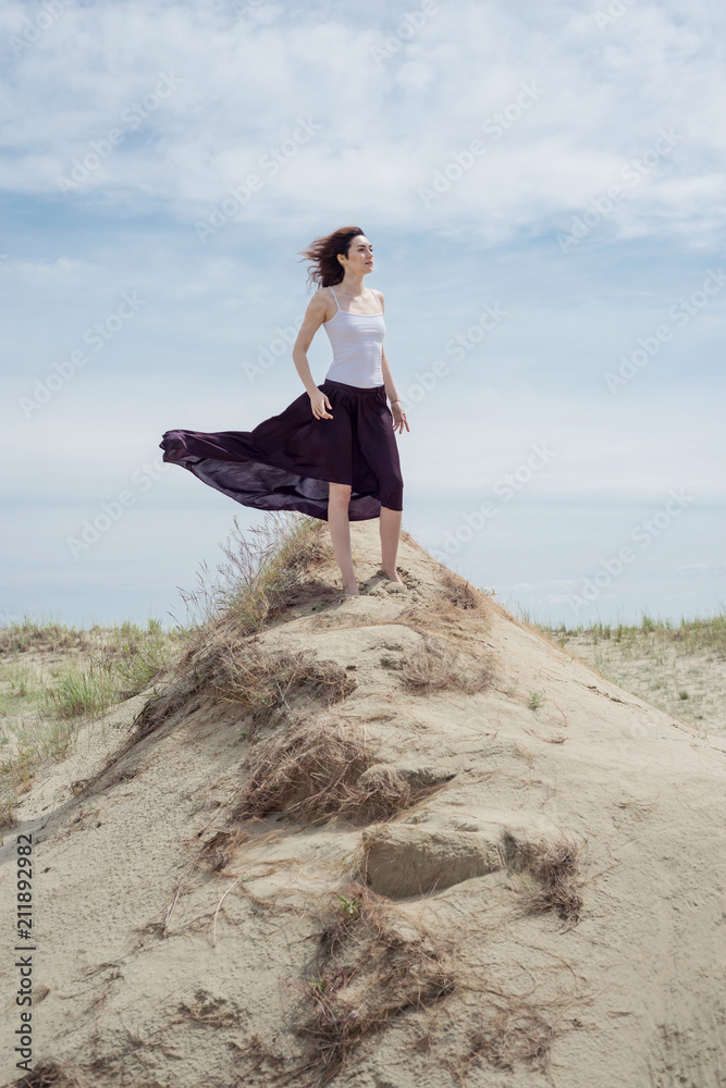 Young woman in a dress standing on a sandy hill holding