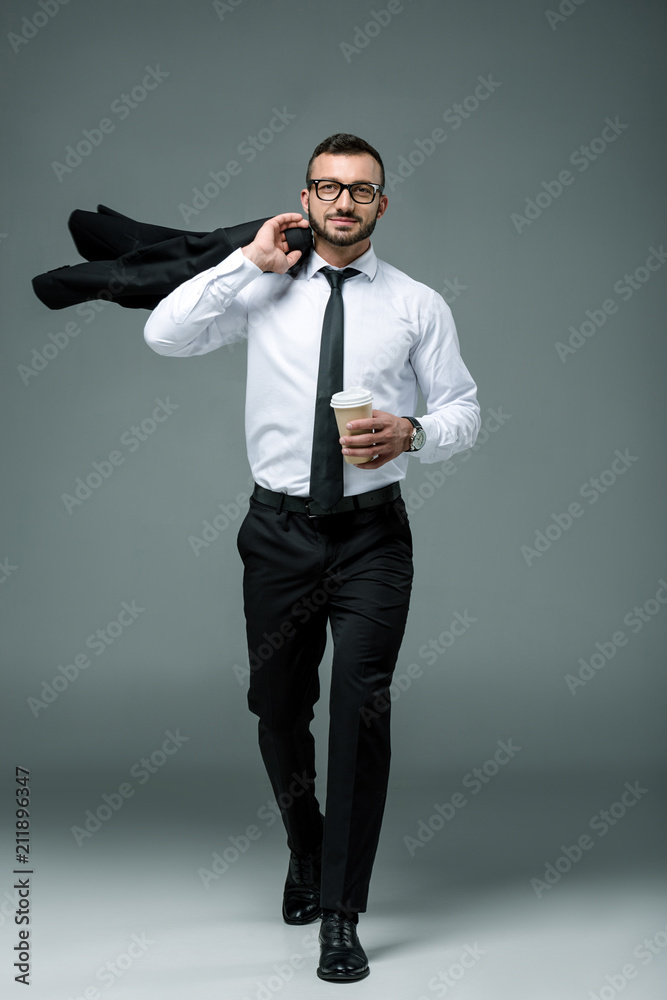 handsome businessman walking with disposable coffee cup on grey