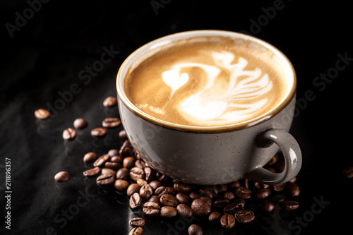 A large cup of expensive ceramics with cappuccino  on top of an art drawing swan from milk. glass on a black mirror background. background image. Copy space