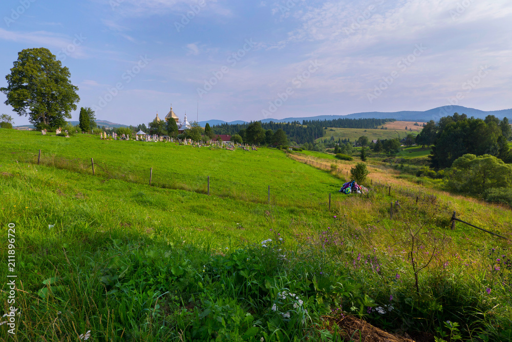 Obraz premium A fenced territory on a green slope on which there is a temple and a cemetery. Onda from the graves is excavated at a great distance from the others
