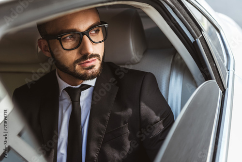 handsome businessman sitting in car and looking away