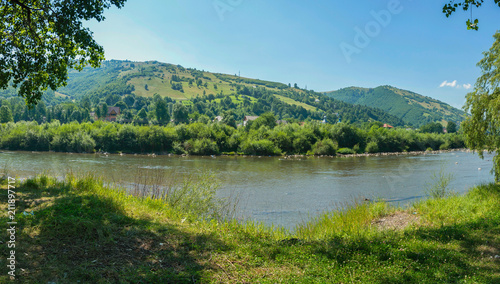 A fast mountain river with huge stones on its way, dividing two green beaches © adamchuk_leo