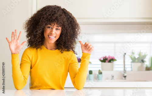 African american woman wearing yellow sweater at kitchen showing and pointing up with fingers number six while smiling confident and happy.