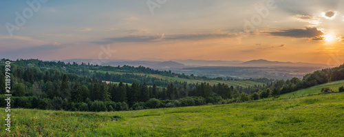 Sunset in the evening sky against the backdrop of green hills and massive vast mountains