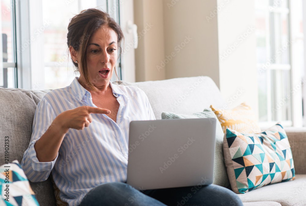 Fototapeta premium Middle aged woman using laptop in the sofa very happy pointing with hand and finger