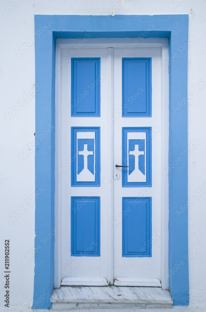 Old blue wooden church door on white wall, Greece
