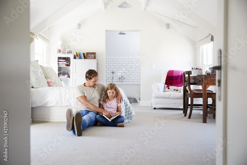 Father and daughter reading a book together in her bedroom
