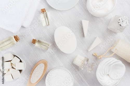 Fresh white natural cosmetics - white cream, oil, towel and bath accessories on soft light white wood table, flat lay.