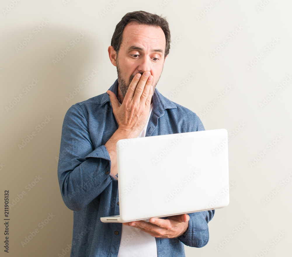 Senior man using laptop computer cover mouth with hand shocked with shame for mistake, expression of fear, scared in silence, secret concept Senior man using laptop computer cover mouth with hand shocked with shame for mistake, expression of fear, scared in silence, secret concept