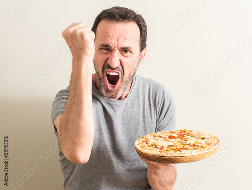 Senior man holding pizza annoyed and frustrated shouting with anger, crazy and yelling with raised hand, anger concept