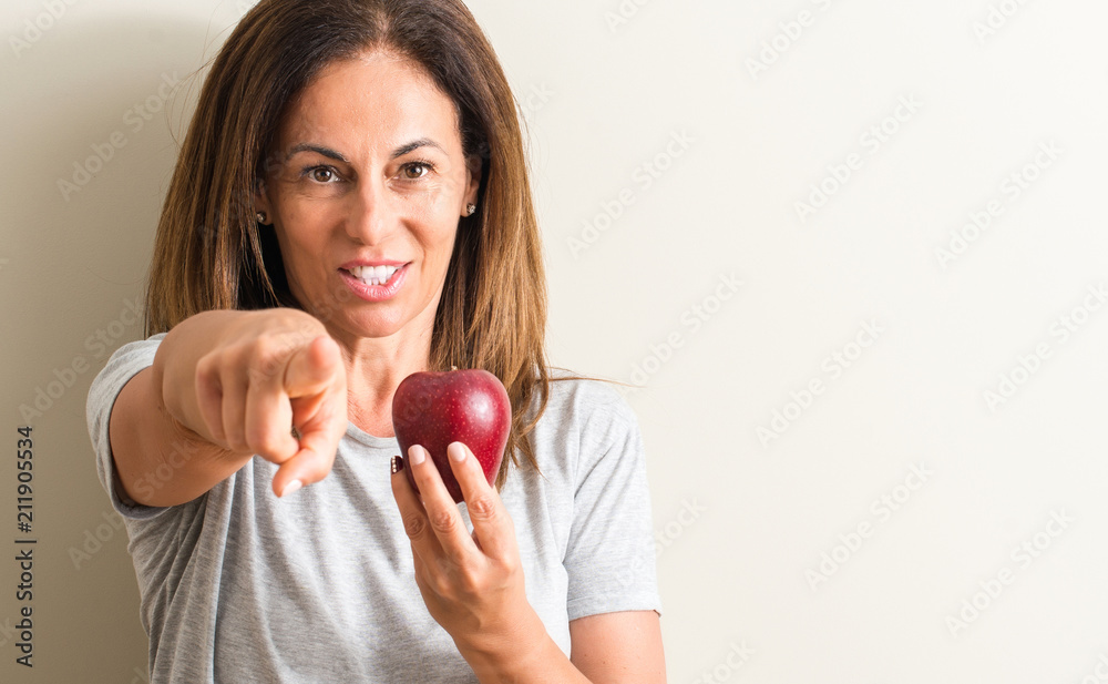Middle age woman holding a green apple pointing with finger to the camera and to you, hand sign, positive and confident gesture from the front Middle age woman holding a green apple pointing with finger to the camera and to you, hand sign, positive and confident gesture from the front