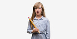 Young blonde child holding big pencil scared in shock with a surprise face, afraid and excited with fear expression