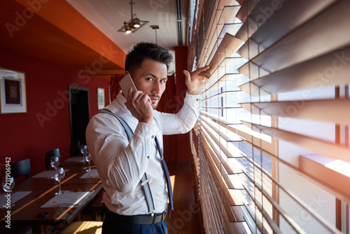 Smiling businessman having mobile phone conversation while standing in office building, happy intelligent man in suit talking on cell telephone photo