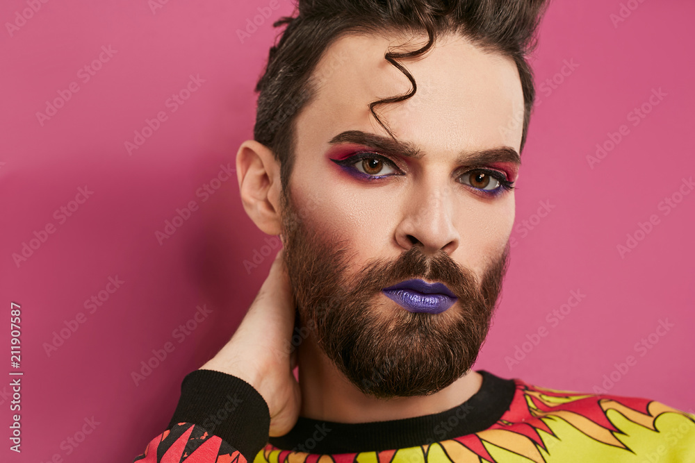 Male makeup look. 3/4 view portrait of a young man rocking beard, quiff,  purple lipstick,