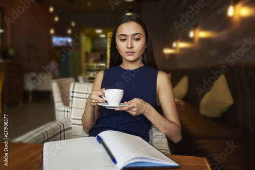 Young lady drinking coffe and looking througha notepad. Attractive business woman lunch in cafe after work. photo