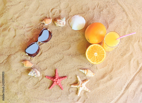 Glass of orange juice, oranges, sunglasses, starfishes and seashells on sand beach