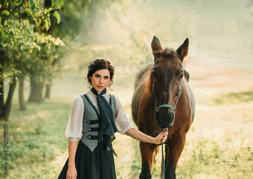 A young lady in a vintage dress strolls through the forest with her horse. The girl has a white blouse, a jabot, a tie, a gray vest, a black long skirt with a train. An ancient, collected hairstyle