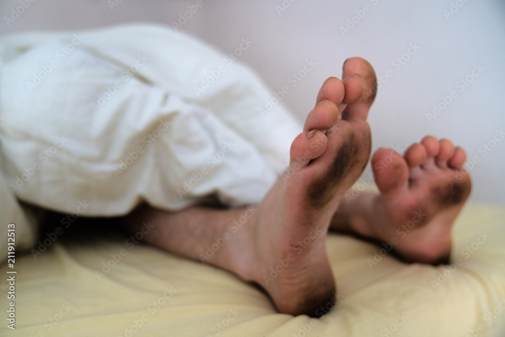 Dirty bare feet of a sleeping person showing out of the blanket on a bed Dirty bare feet of a sleeping person showing out of the blanket on a bed