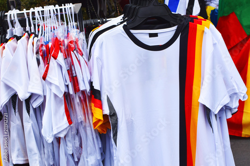 Football fans accessories white t-shirts with colors of german flag stand on street for sale.