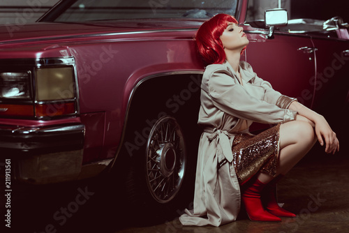 beautiful stylish young woman with closed eyes crouching near vintage car