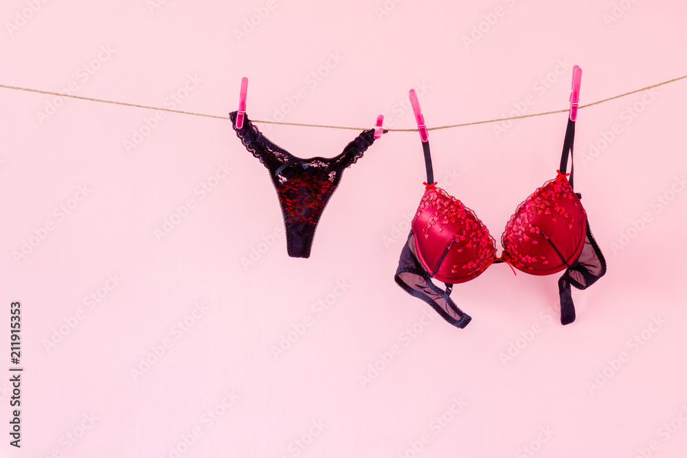 Woman's clean red bra and black panties. Underwear drying on laundry rope  at pink wall. Lingerie's preparing for date night. Dry cleaning. Regular  washing. Clothes care. Stock Photo