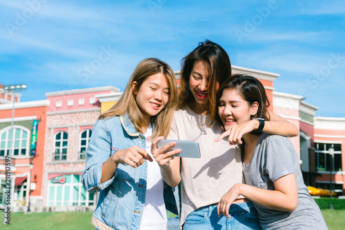Group of young Asian Women selfie themselves with a phone in a pastel town after shopping. Young women group do outdoor activity under the blue sky. Outdoor activity after shopping concept.