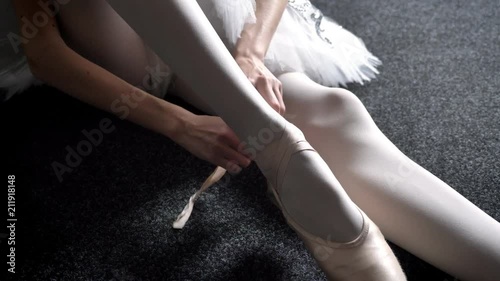 Girl ballerina ties ribbon on pointe, sitting on floor, ballet concept