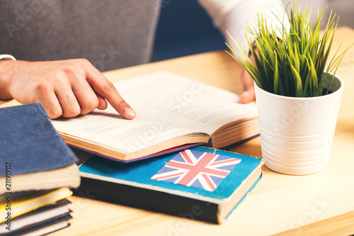 Man reading book at the table full of books, English language learning concept