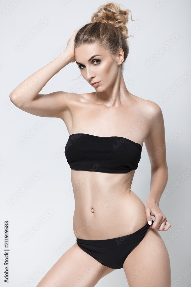 Foto de Sexy young girl in a black bikini on a gray studio background.  Sports girl in a black swimsuit. do Stock