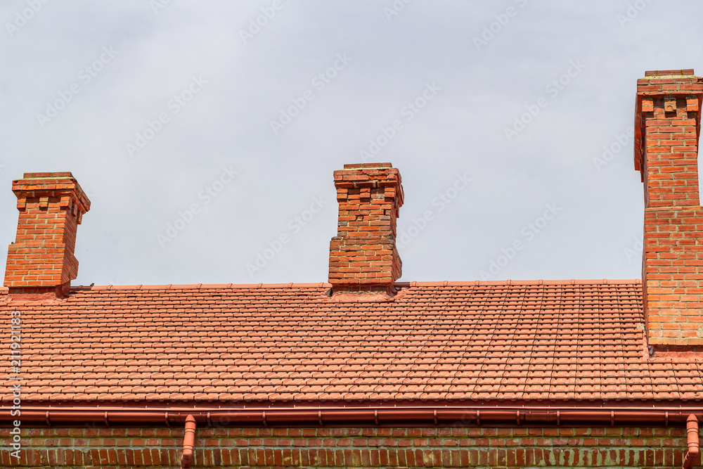 Naklejka premium Roof covered with new tile, with chimneys made of bricks against the background of a cloudy sky