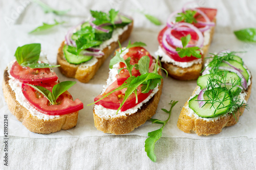 Bruschetta or sandwiches with tomatoes, cucumbers and cream cheese, decorated with greens.