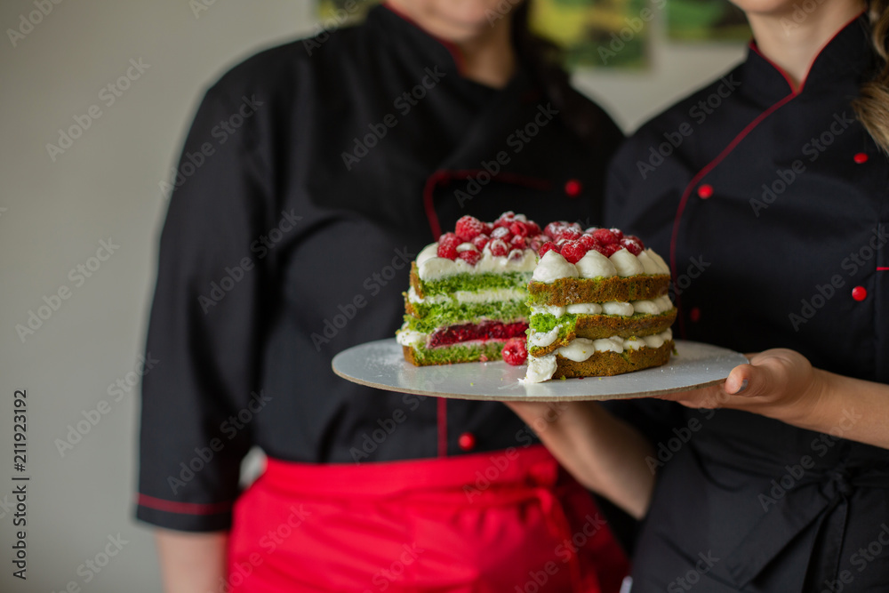 Confectioner women  in  Red and Black  Work Uniforms Holding the Cake with Berries  in the Kitchen. Confectioner, Cake, Cooking.
