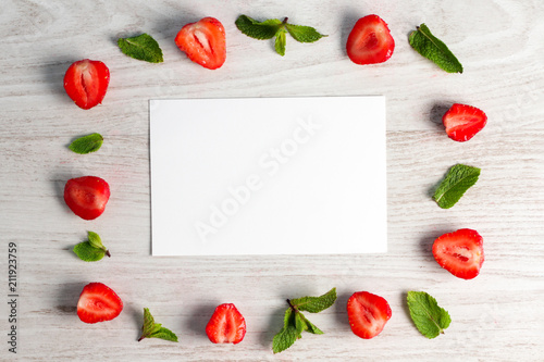 Frame for text made from strawberries and mint leaves on a wooden white background. Copy space.