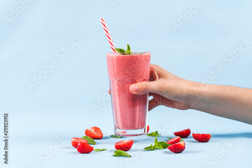 A glass of strawberry smoothie with mint in hand on a blue background