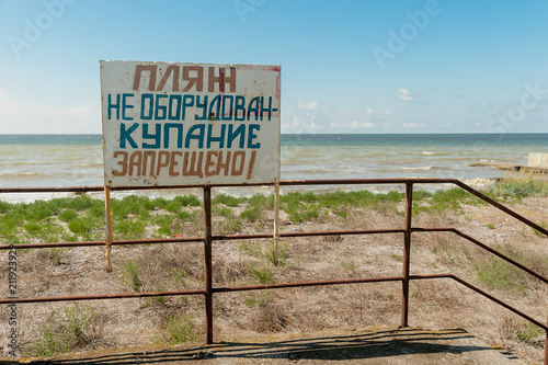 Warning sign on the shore. Text in Russian: the beach is not equipped. swimming is forbidden