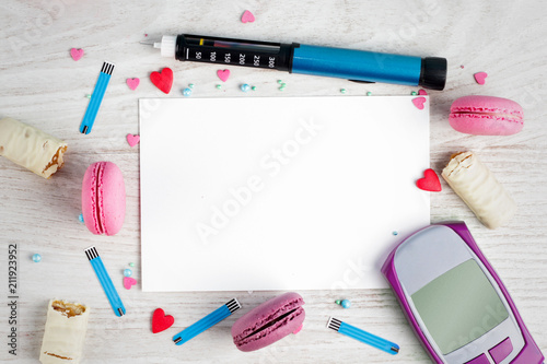 Frame for text from Sweet macaroons, insulin pen, glucometer, blood sugar check strips, chocolate bar and sweet powder on a wooden white background. Copy space.
