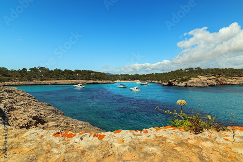 Sea coast scenery with blue turquoise waters in Majorca island. Anchored boats in Cala Mondrago beach Balearic Islands. Spain getaway vacations concept.