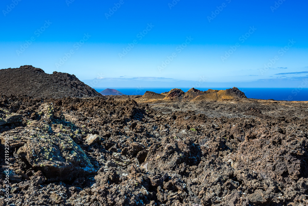 The vast emptiness and loneliness of the Lanzarote black frozen lava volcanic desert with the blue waters of the Atlantic Ocean in the background