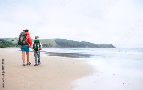 Walking travel with child. Mother and son walks together on sandy beach on the famous Camino del Norte Way, Spain