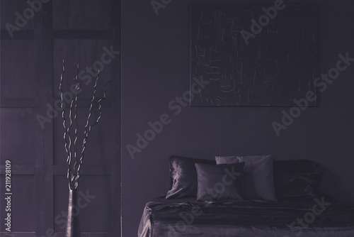 Metal dekor next to bed in dark unicolor bedroom interior with mockup of poster. Real photo