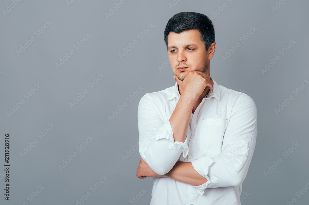 Indoor shot of handsome brunet man with pensive expression, dressed in white shirt, tries to find solve a problem isolated on grey background with copy space. Business Lifestyle Emotion Indoor shot of handsome brunet man with pensive expression, dressed in white shirt, tries to find solve a problem isolated on grey background with copy space. Business Lifestyle Emotion